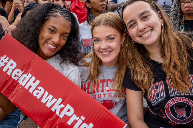 Three students smiling holding a #RedHawkPride banner. 