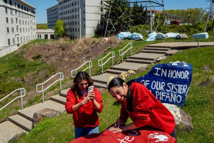 Two students putting their painted white hand on a red Montclair rock.