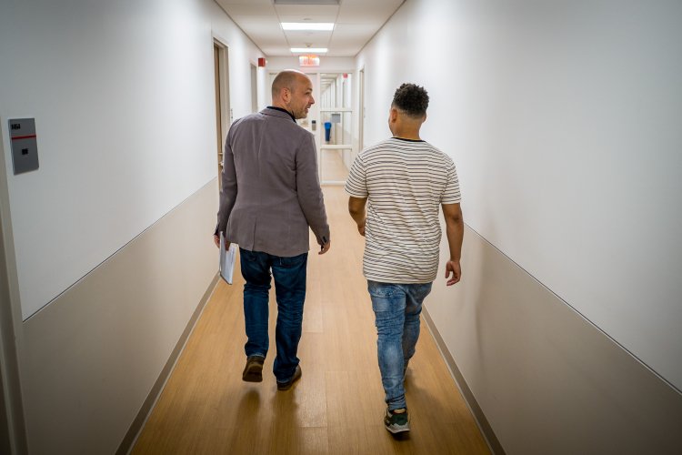 A student and professor talk while walking down a hallway.