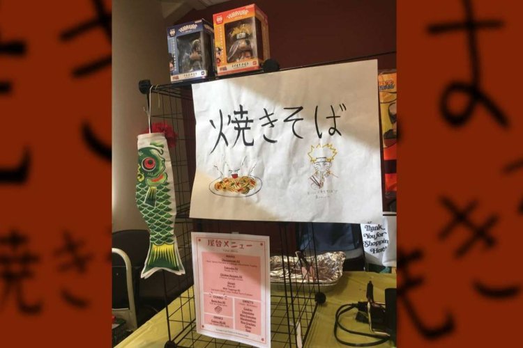 Japanese food booth display with a hand-drawn “焼きそば” (yakisoba) sign, menu, carp streamer, and anime-themed decorations