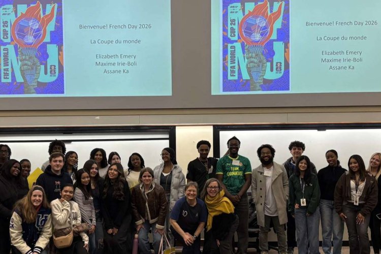 A large group of college students pose in front of two project screens in a classroom