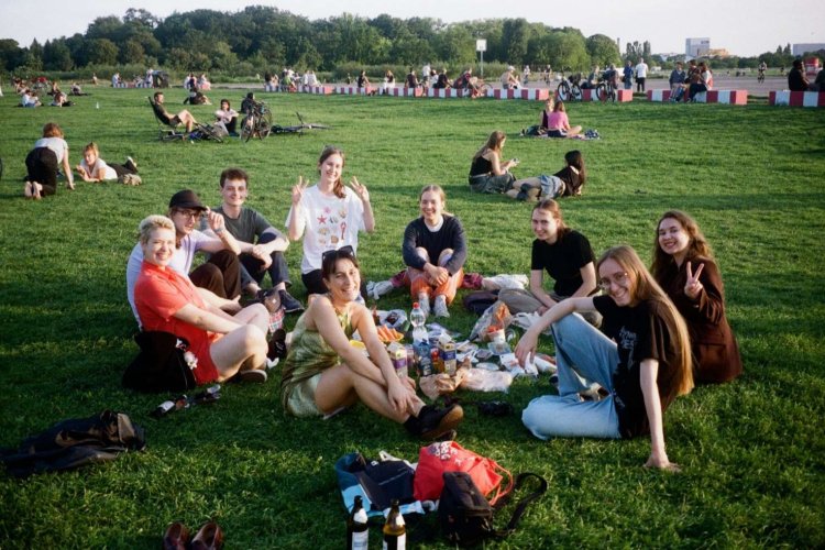 A group of college students sit on the grass in a circle in a large field