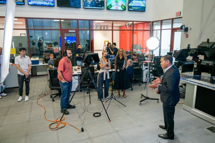 Rob Nelson, anchor of “NJ PBS News with Rob Nelson,” talks to a camera surrounded by faculty and students in newsroom. 