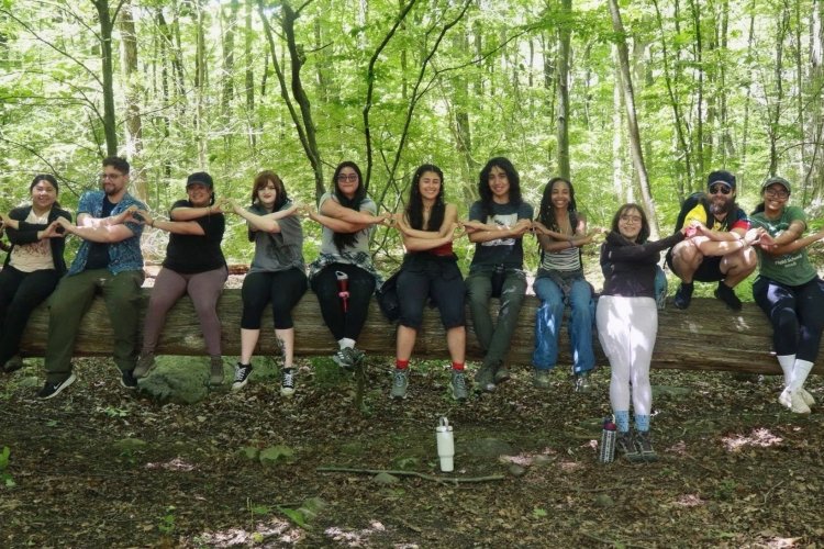 photo of field school students sitting on a fallen tree log, interlocking arms and using hands to make hearts