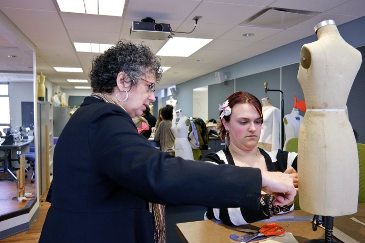 An instructor and a student work with fabric and a dress form in a fashion-design classroom.