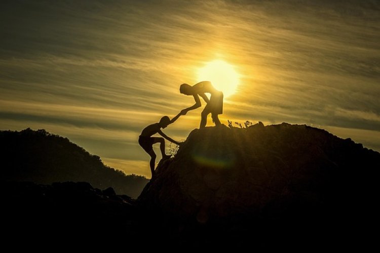 A person helps another person climb a mountain.