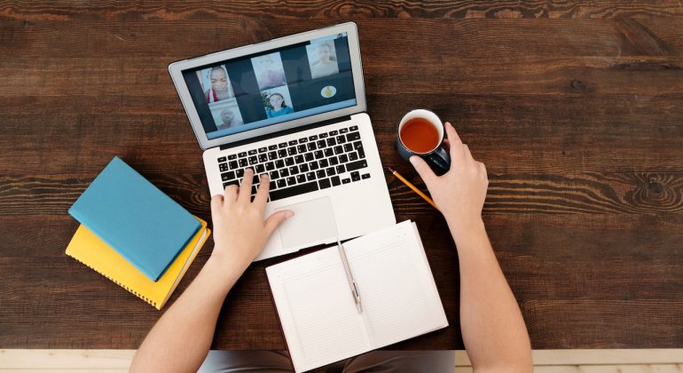 person sitting at computer with open notebook and a tea