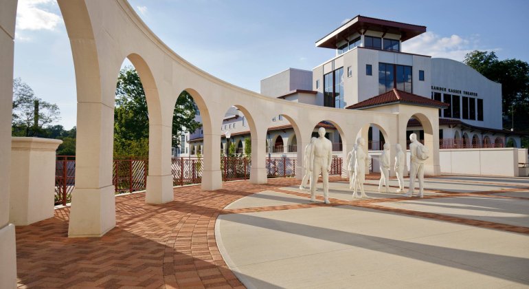 Late-day view of an arched promenade with long shadows and a nearby statue installation.