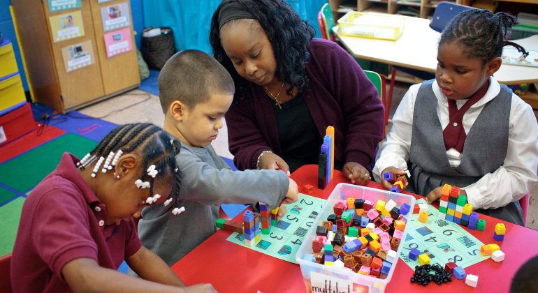 a teacher shows 3 kids how to do math