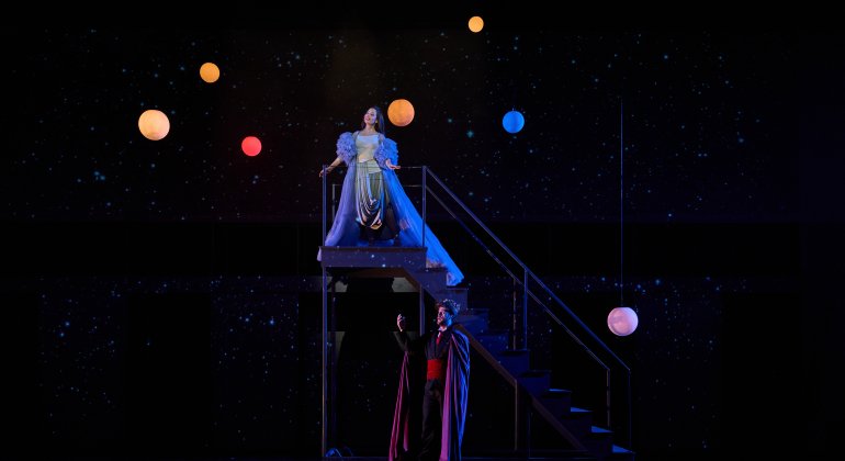 Two opera performers on stage with colorful globe lights floating 