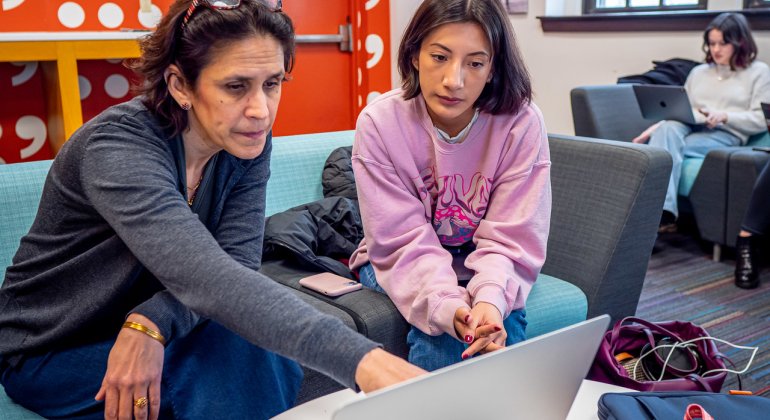 Professor George teaches a student at her laptop during a media course.