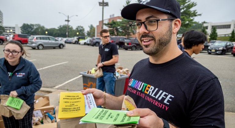 Commuter Life staff memeber hand out welcome bags and event flyers to students in a campus parking lot during a commuter appreciation event.