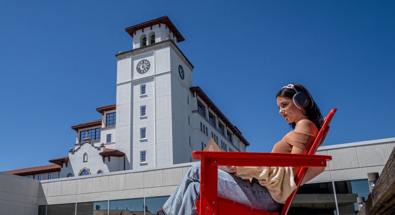 student sitting in red Adirondack chair in front of university hall