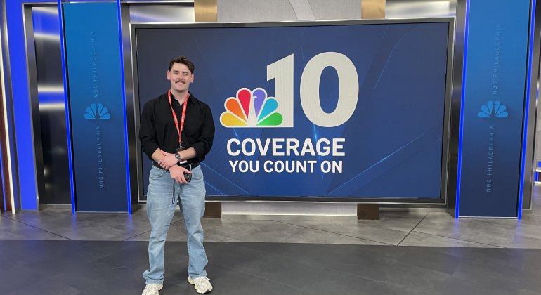 Recent mentoring program graduate visits NBC10 studio and poses in front of network signage.