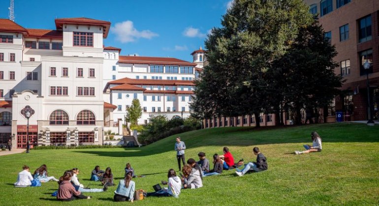 A college class sits on the lawn of a college campus