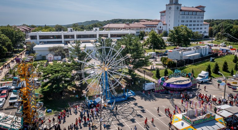 An aerial view shows students enjoying carnival rides and activities during a campus event with University Hall in the background.