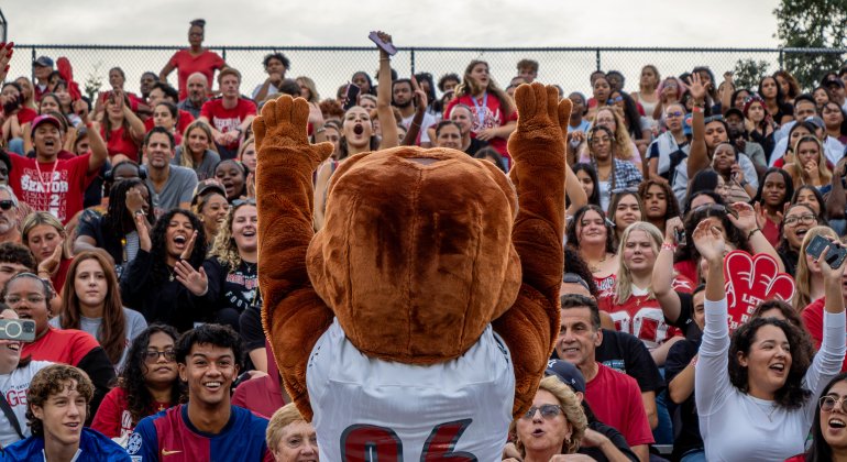 Rocky the Red Hawk mascot with a football jersey on in front of a crowd. 