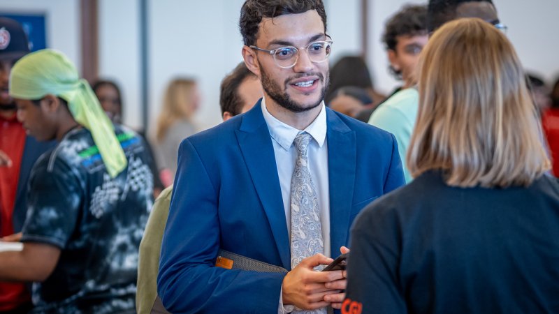 Student wearing a suit networks with an employer at a Career Fair.