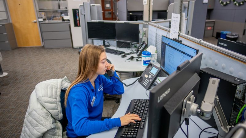 A student working on campus. She is sitting at a computer with her hands on the keyboard and she is on the phone.