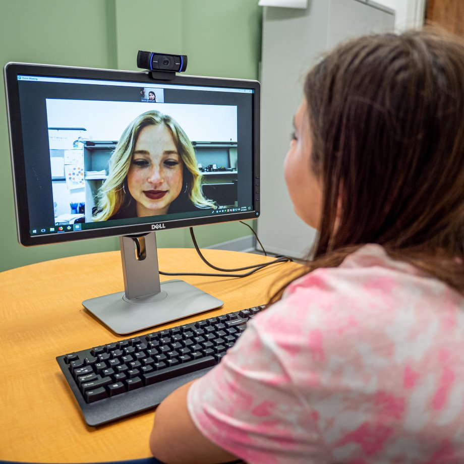 A girl looks at a computer monitor where she is on a video call with a psychology student