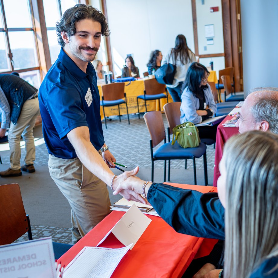 man shakes hands with reps from school district at career fair