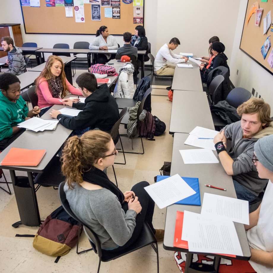 Groups of college students sit around a classroom discussing an assignment
