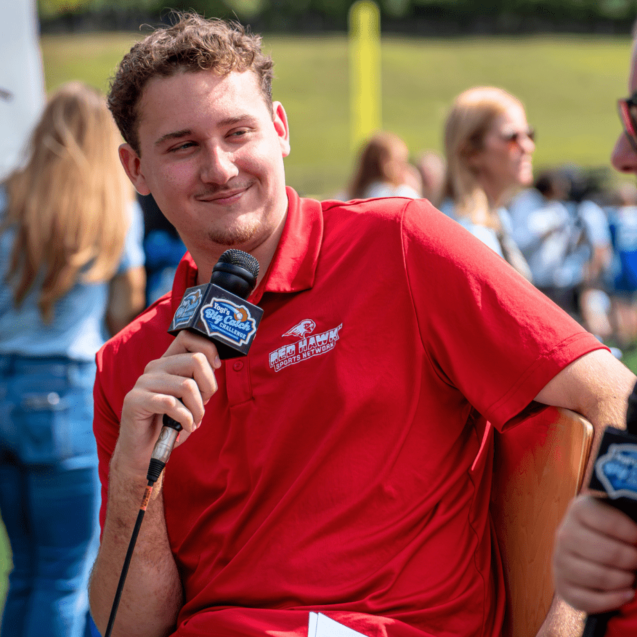 Student holding mic listening to another student on his right speaking at the Yogi Berra stadium.