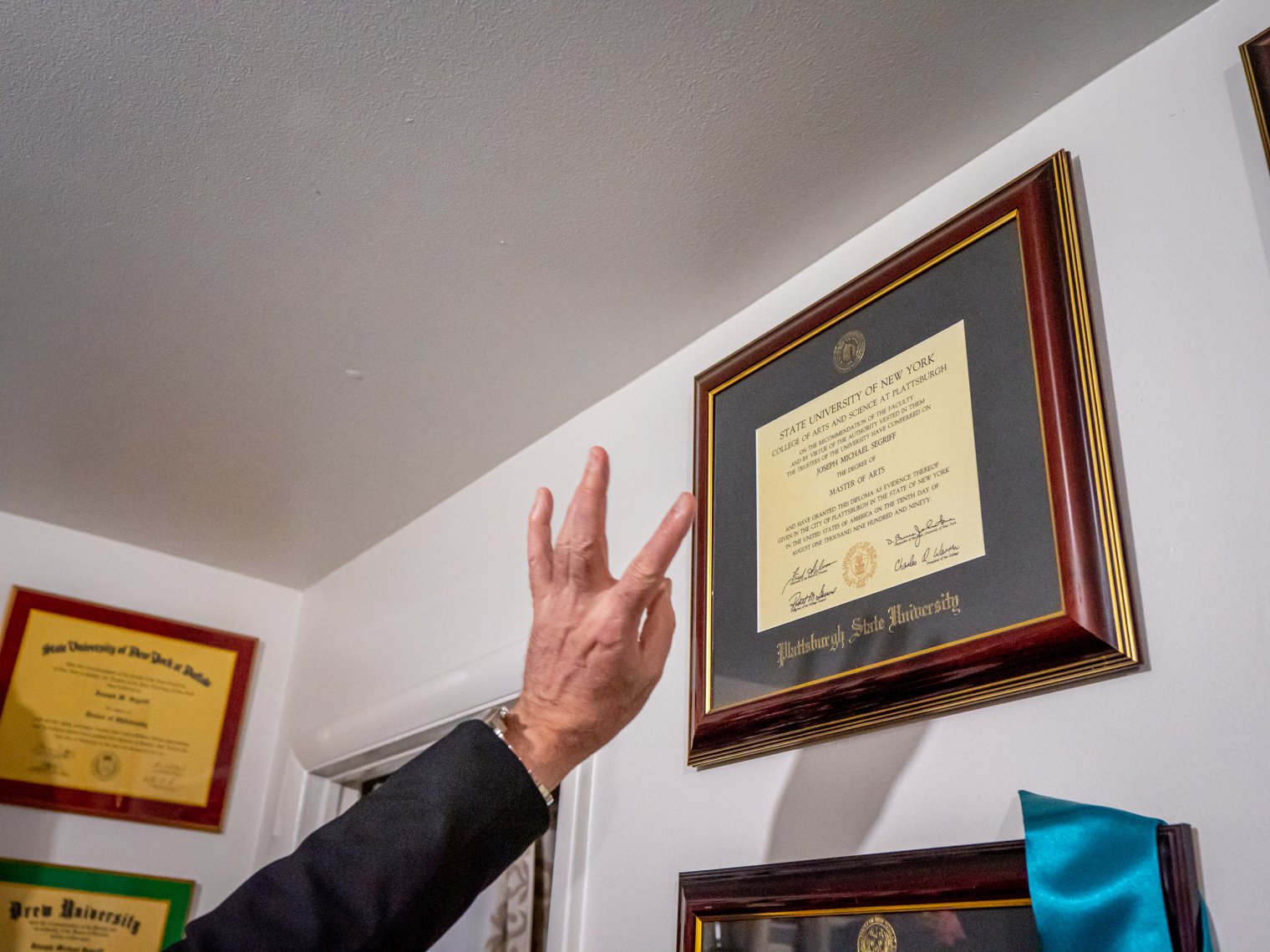  A man’s hand points to a diploma on a wall.