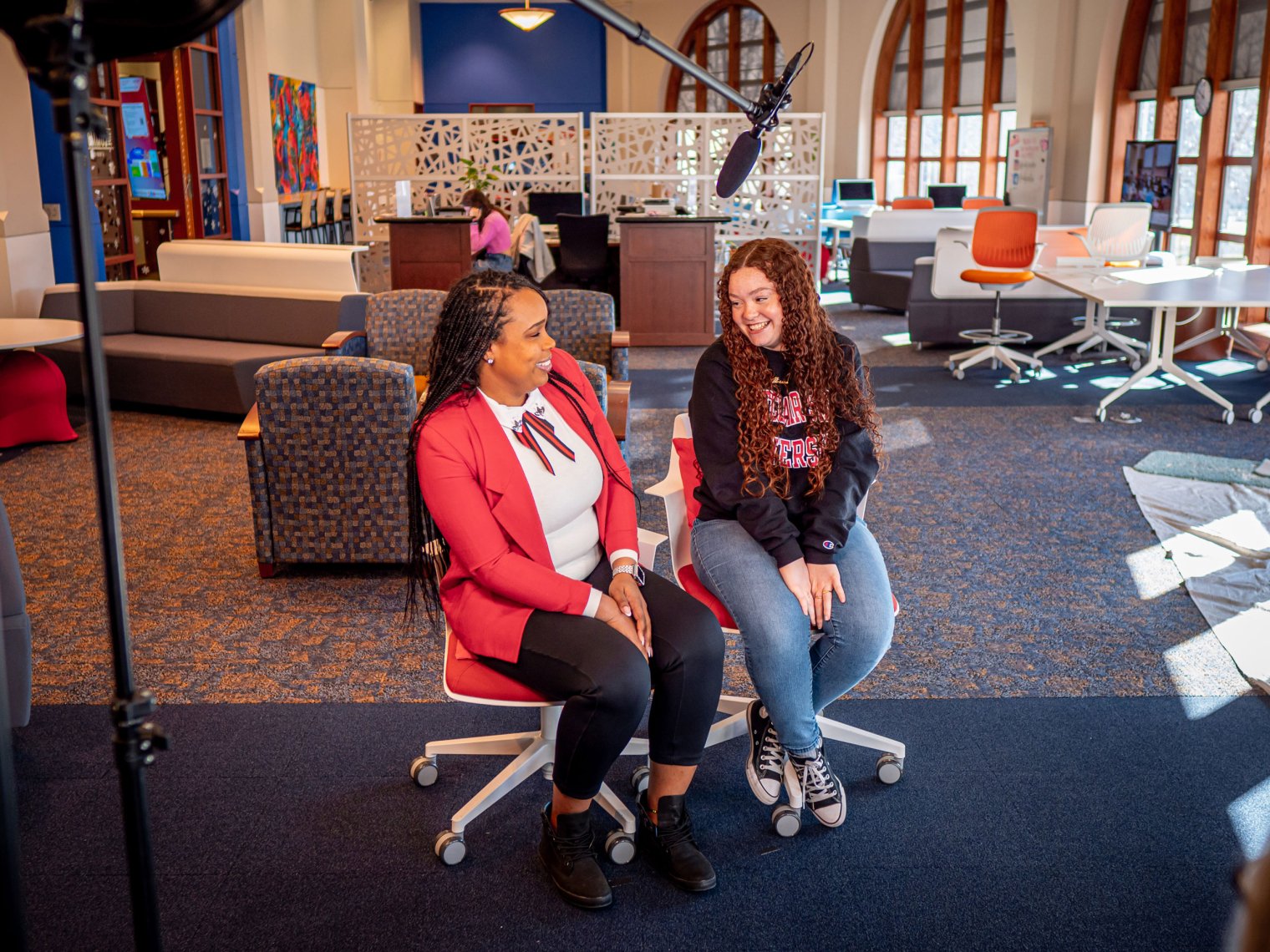 Two women sit in a large room with a microphone above them.