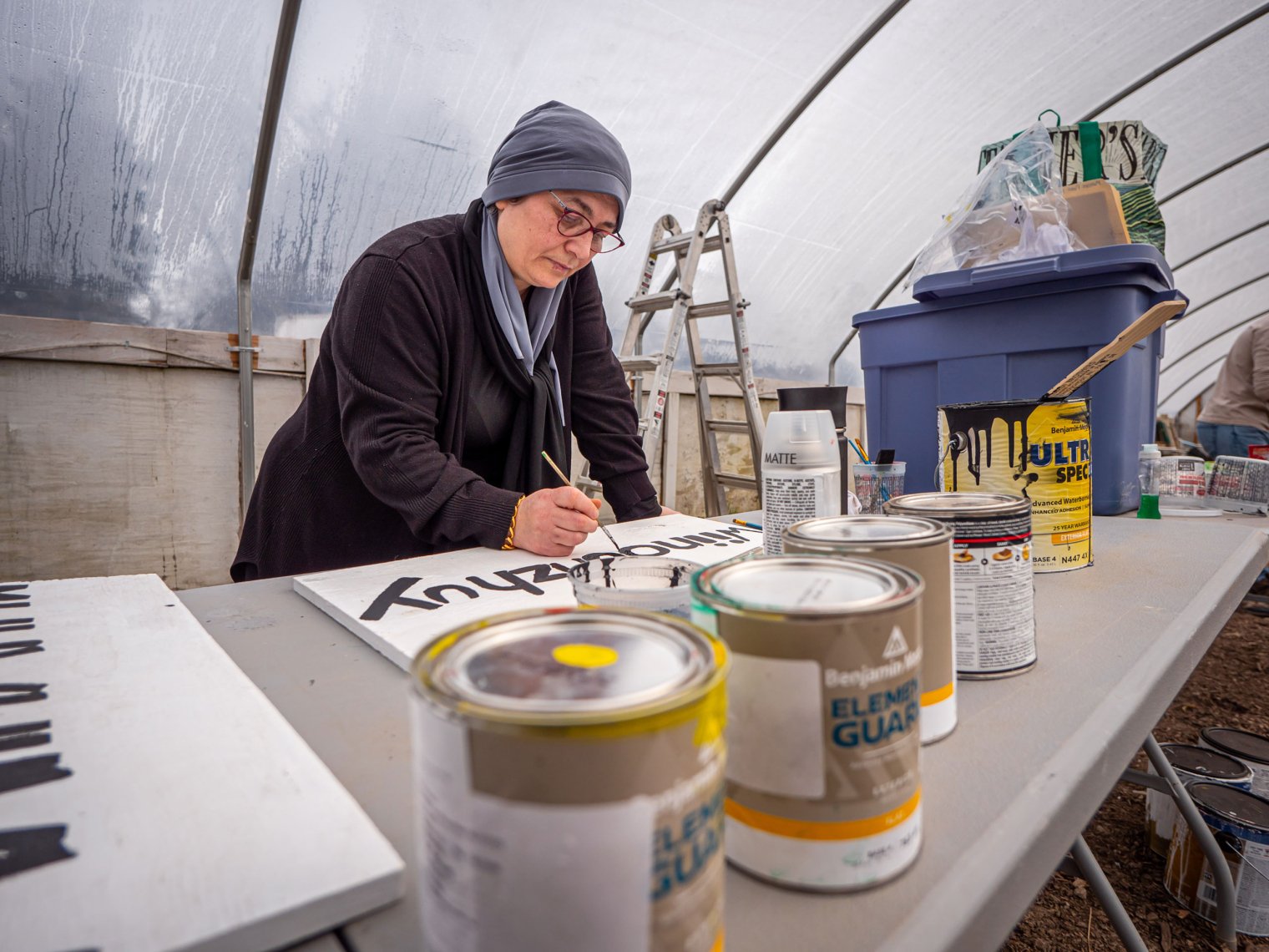 Female paints lettering on a sign.