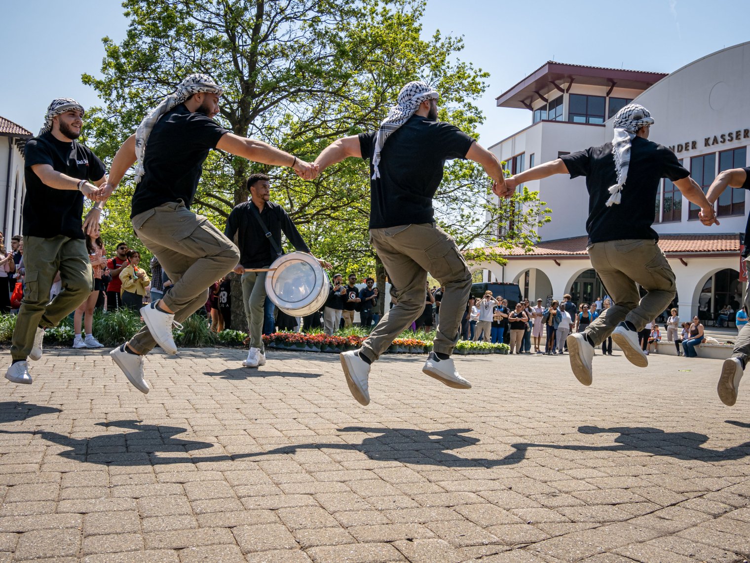 Men holding hands jumping as they are wearing traditonal clothing.