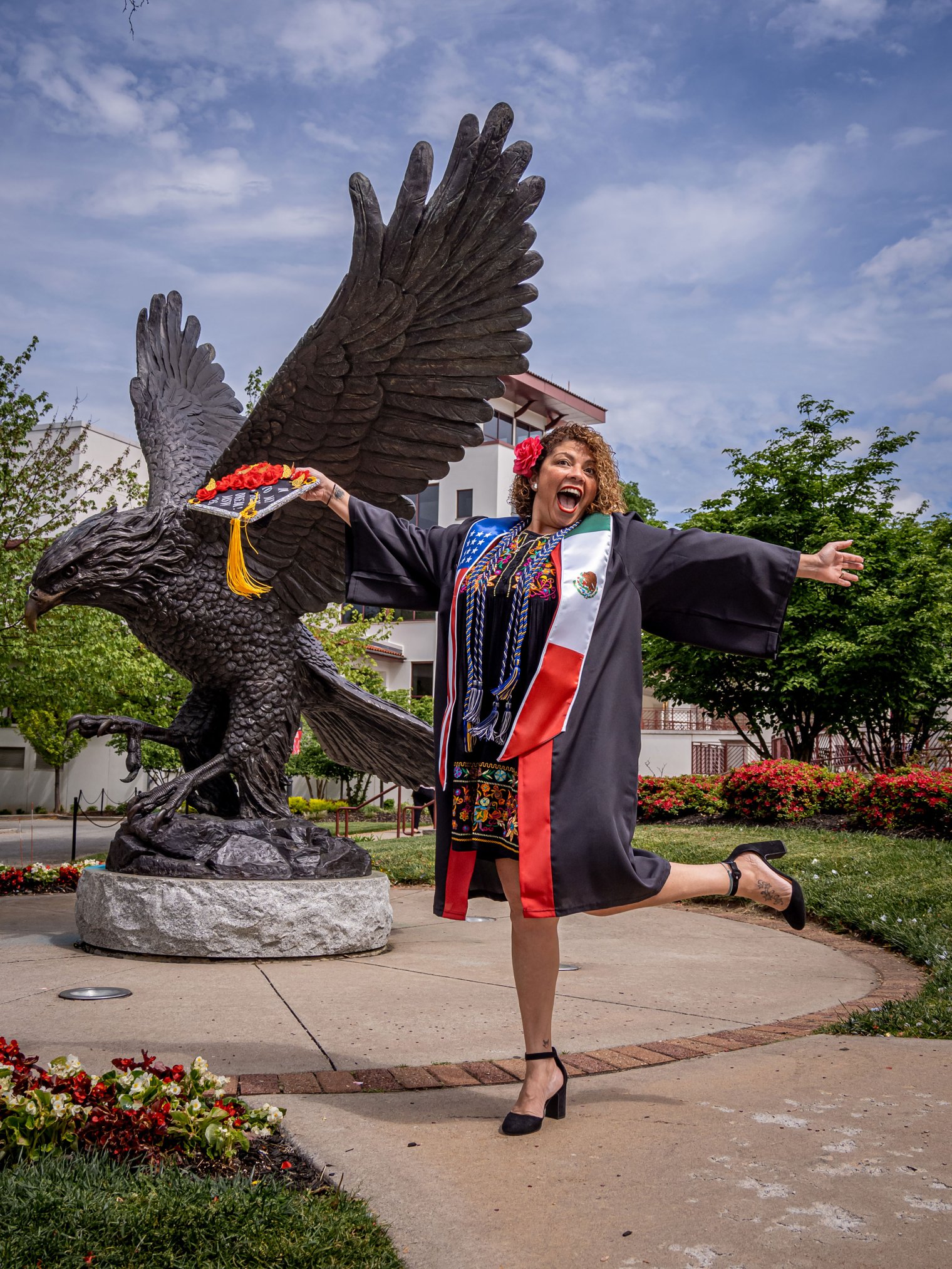 Graduate Iliana Woodhull celebrates in front of the Red Hawk statue.