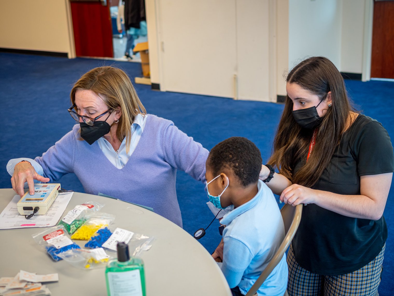 Professor Maryrose McInerney, Alyssa Bonapace sit with student preparing otoacoustic emission test