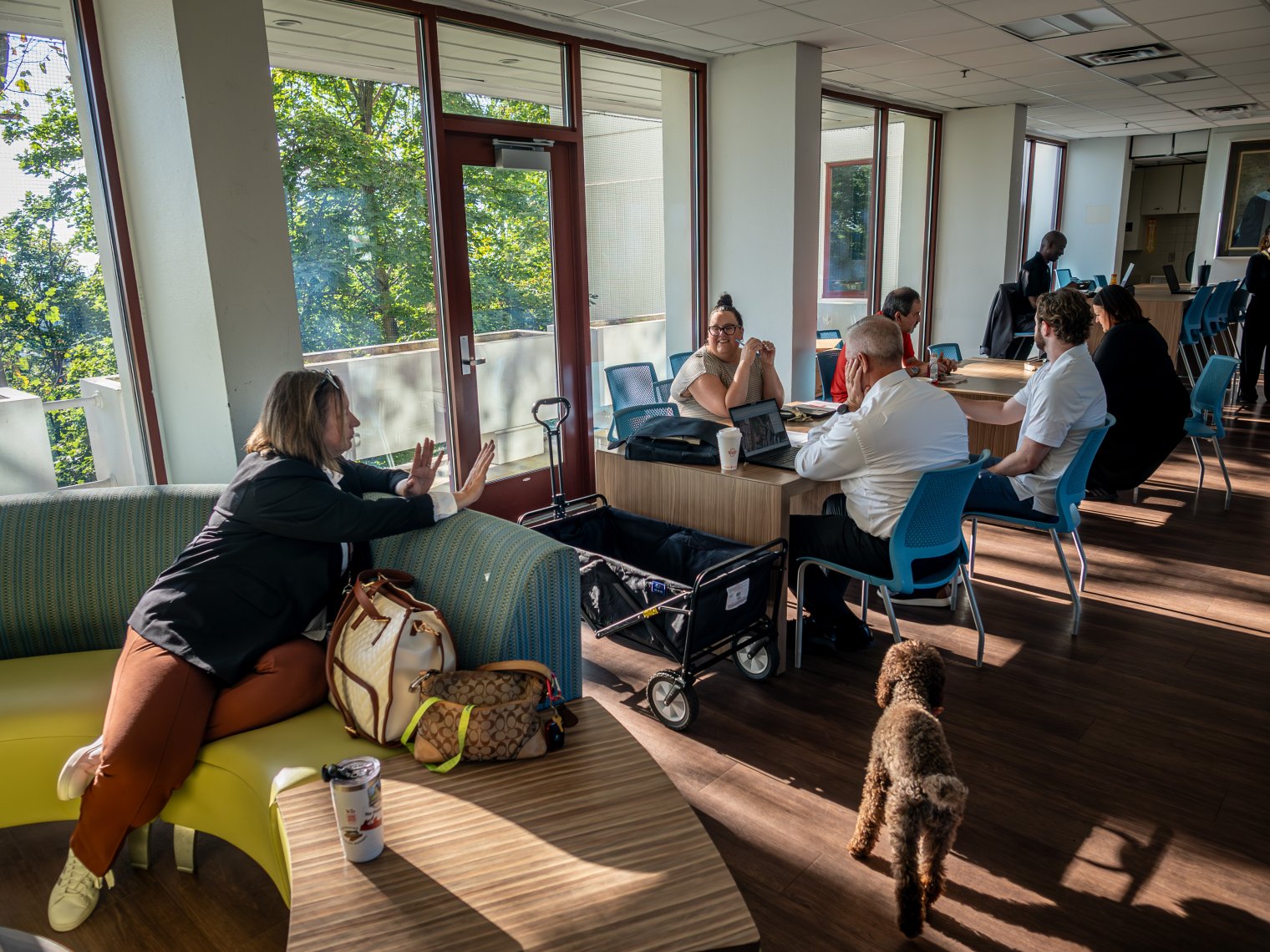 Monica speaking to a group of people while sitting down over a couch, everyone else is sitting down on a laptop on a desk.