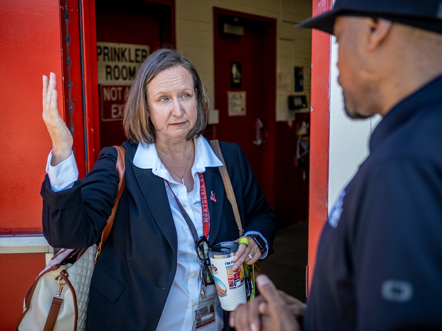 Monica discussing with another gentleman while she gestures upward and a coffee in her hand.