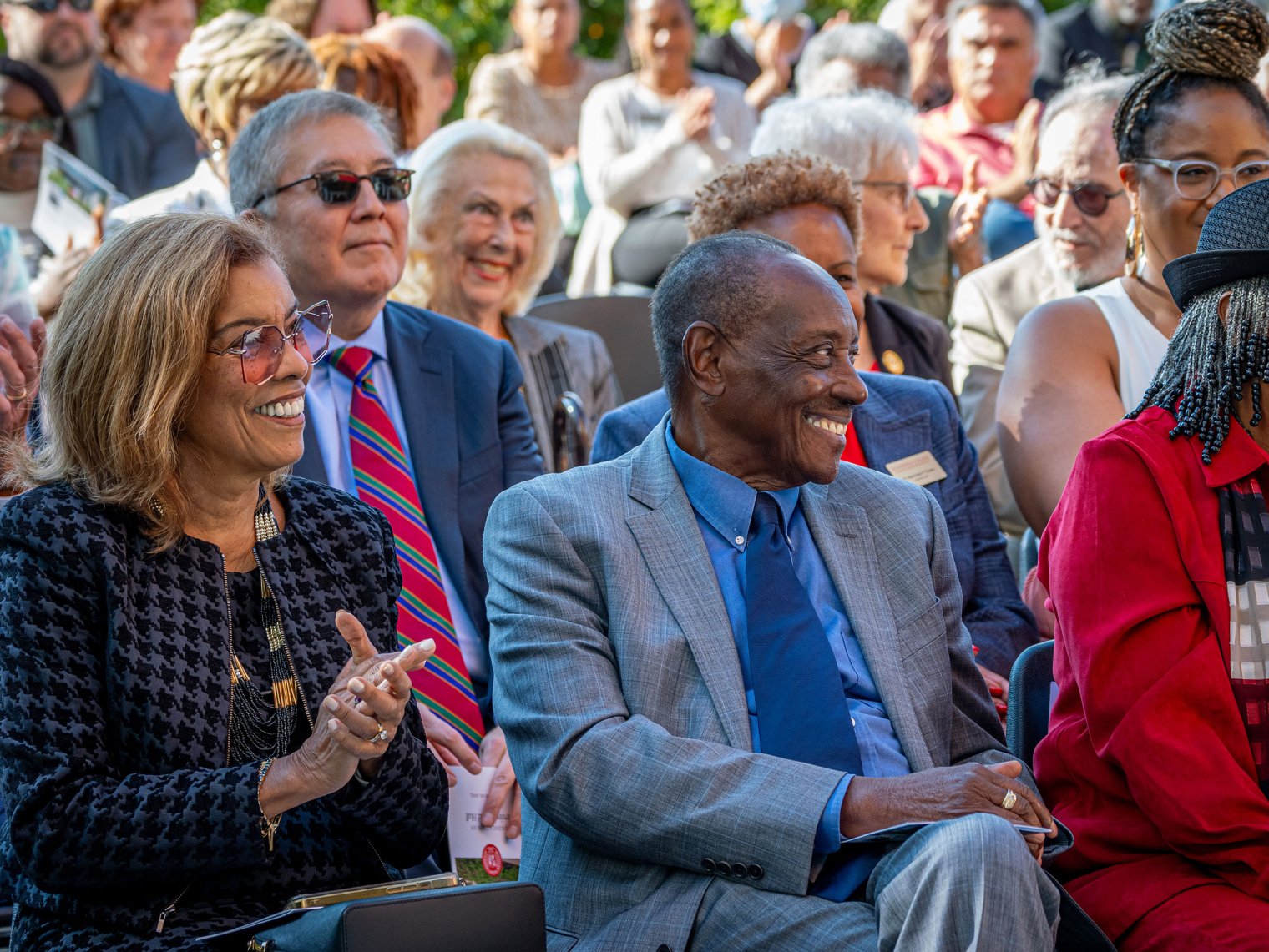 A man and a woman smile with a crowd of smiling people behind them.