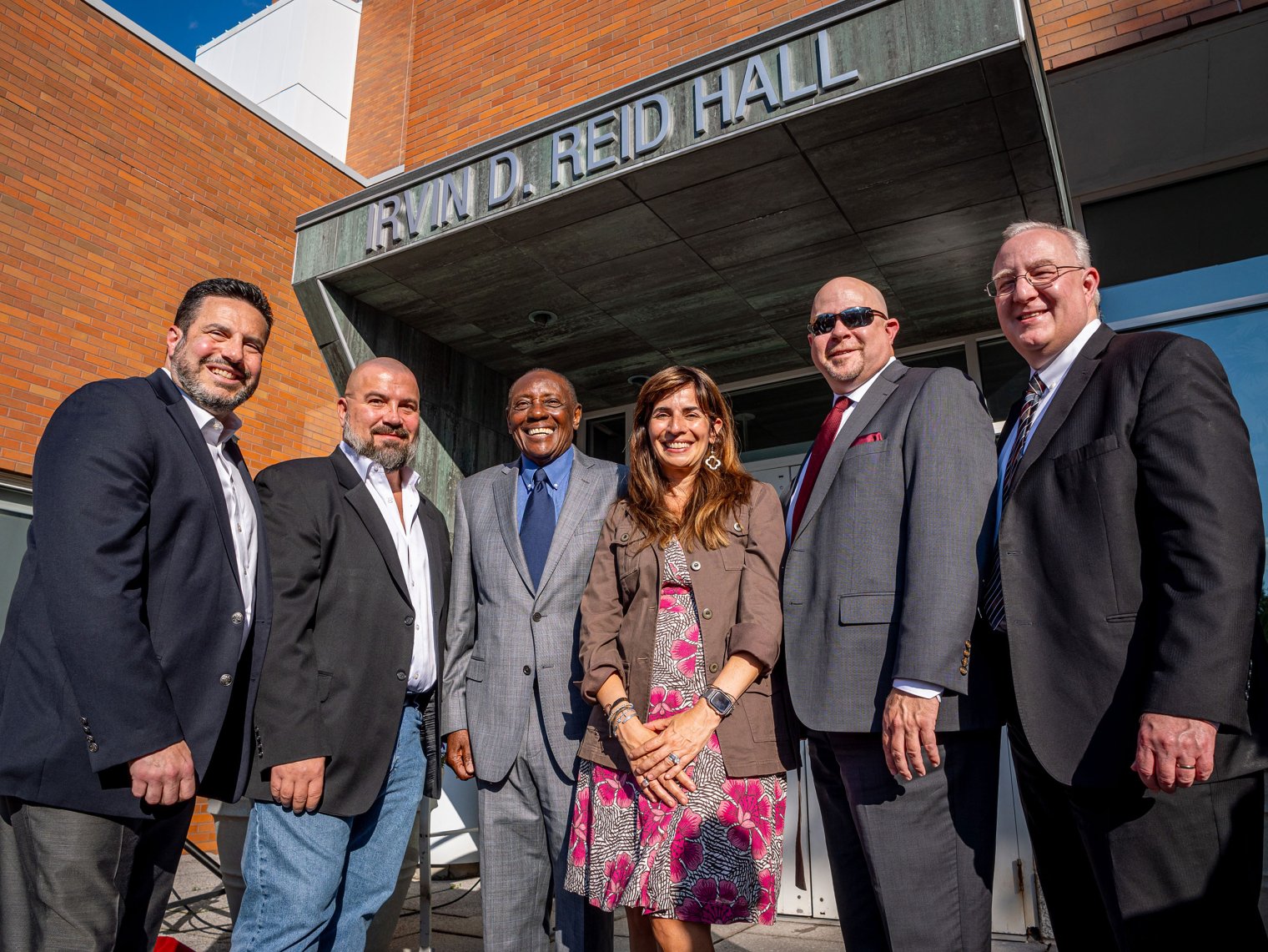 Six people stand in front of the sign that says Irvin D. Reid Hall