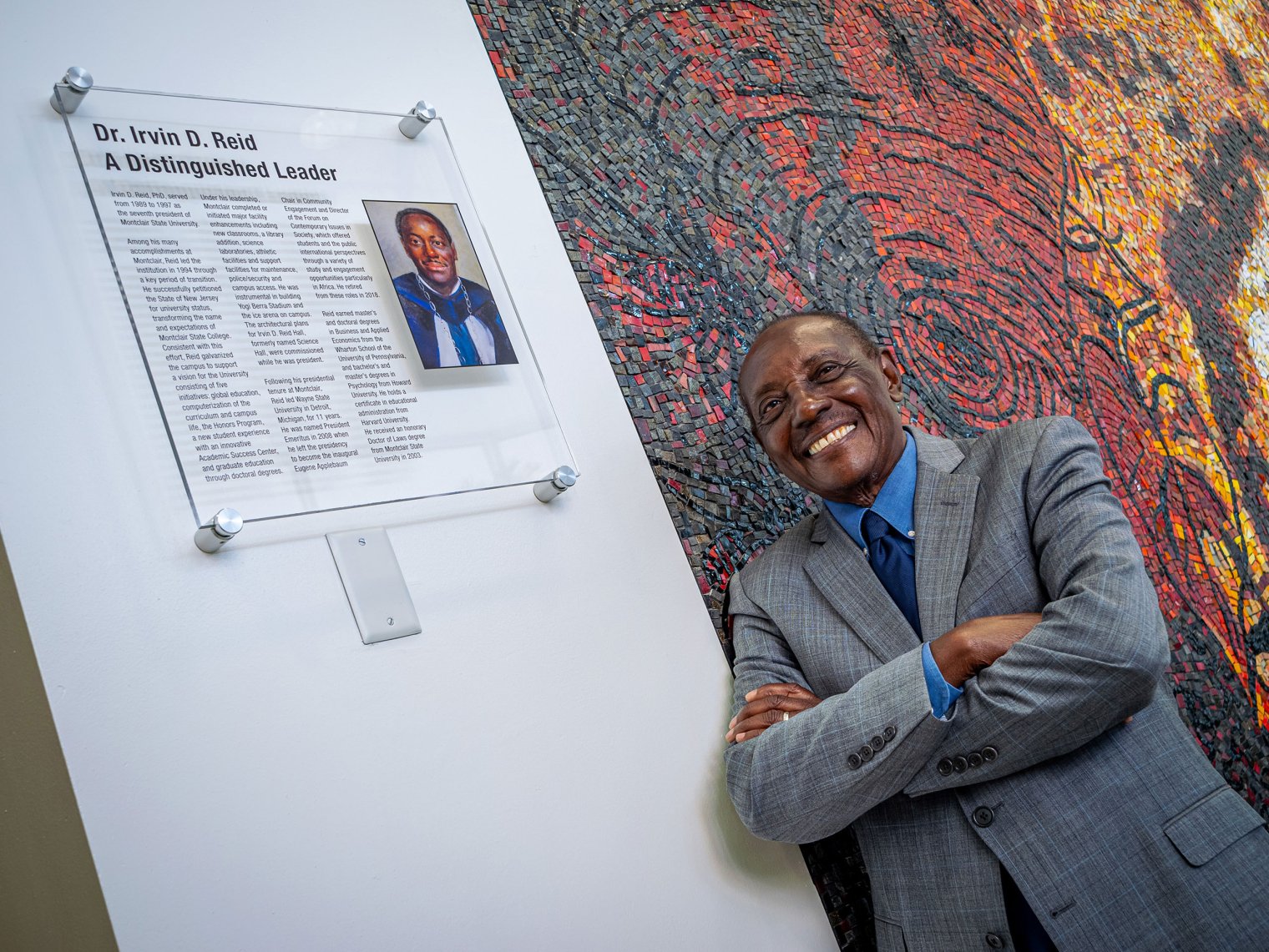 Irvin D. Reid stands in front of a plaque that says Dr. Irvin D. Reid, A Distinguished Leader.