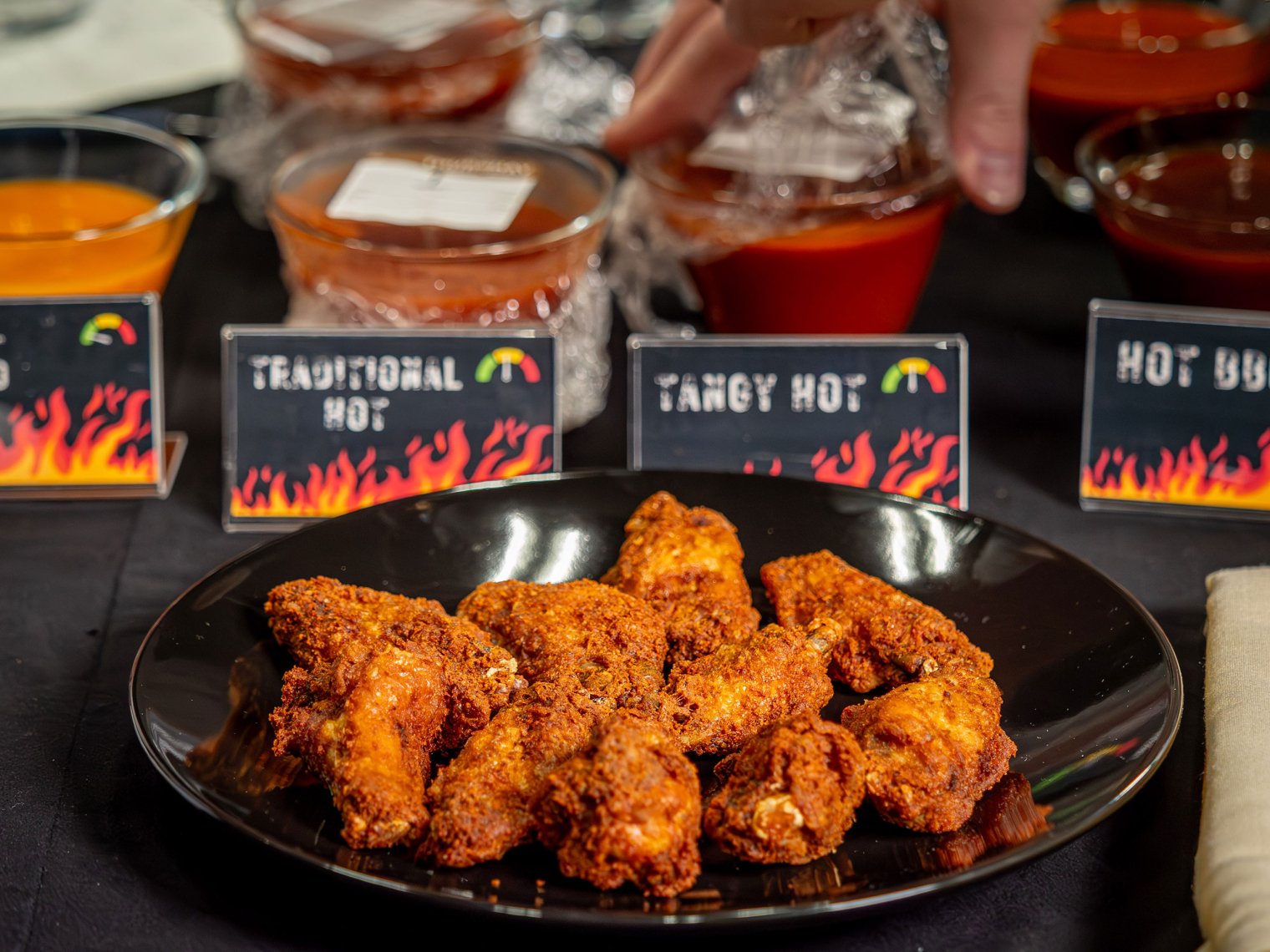 A plate of chicken wings with spicy sauces behind them.
