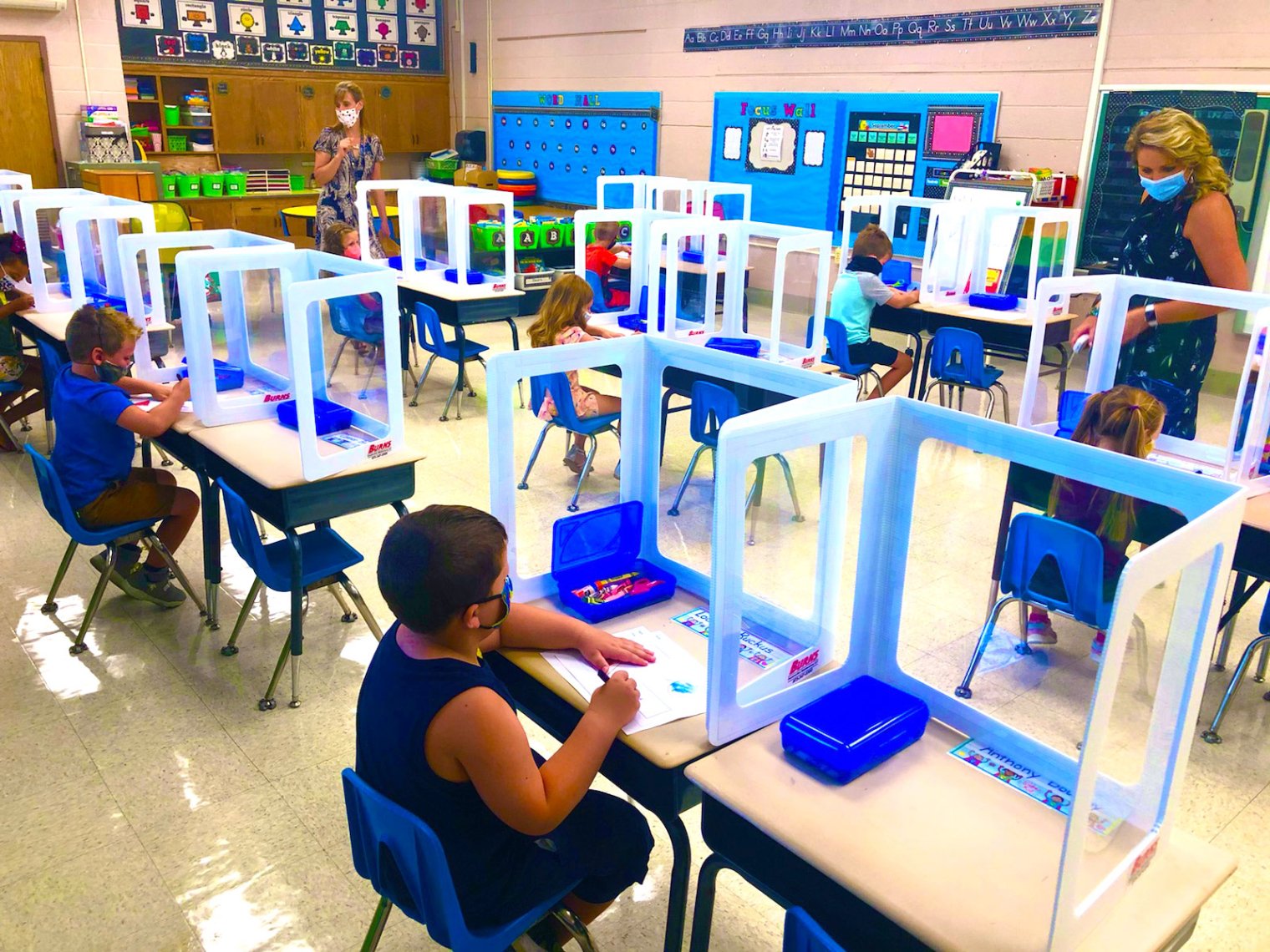 wide view of elementary school classroom with spaced desks and plastic dividers