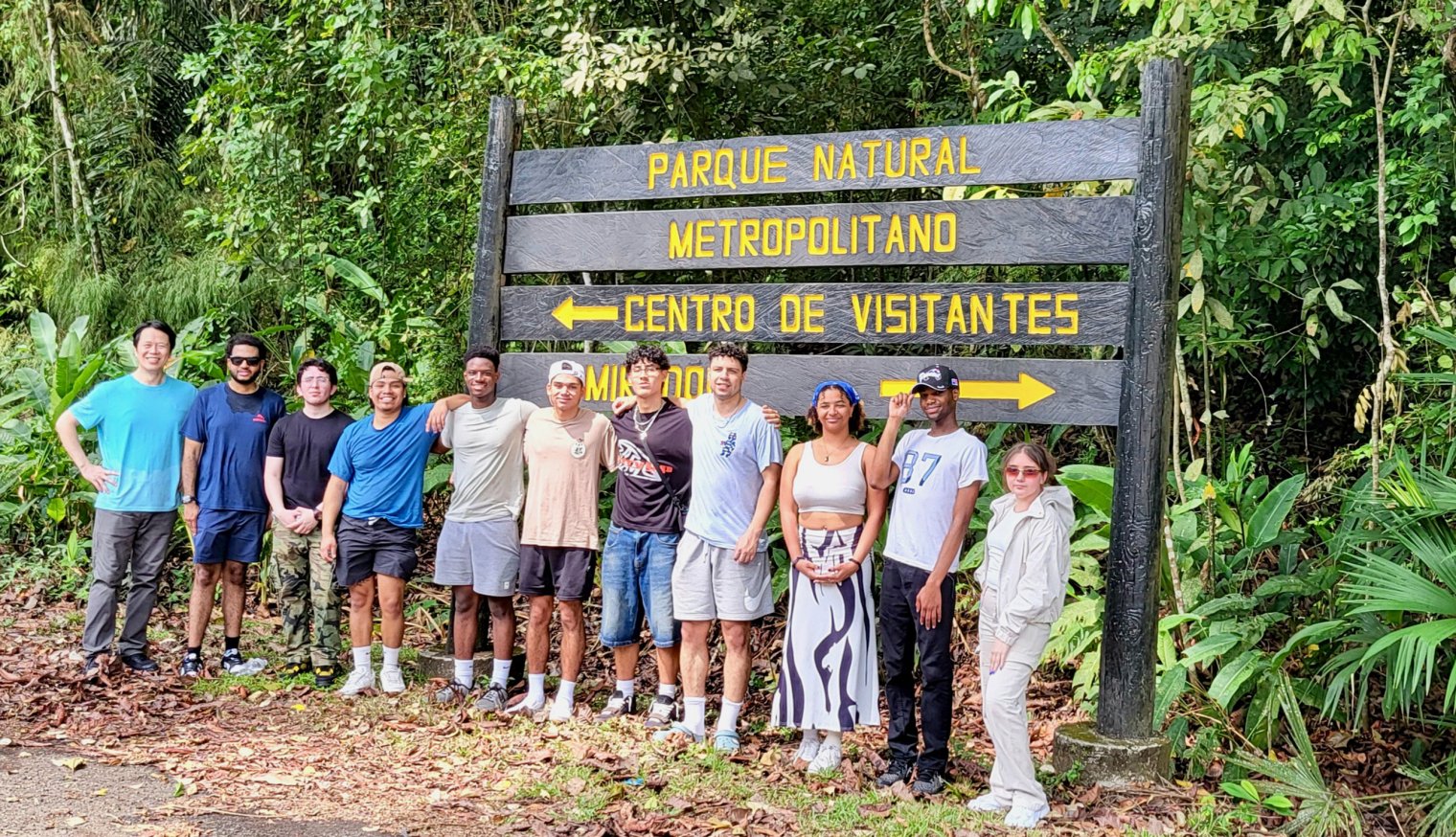 A group of Montclair students and faculty stand together in front of the entrance sign to a tropical forest sanctuary in Panama City, surrounded by lush greenery.