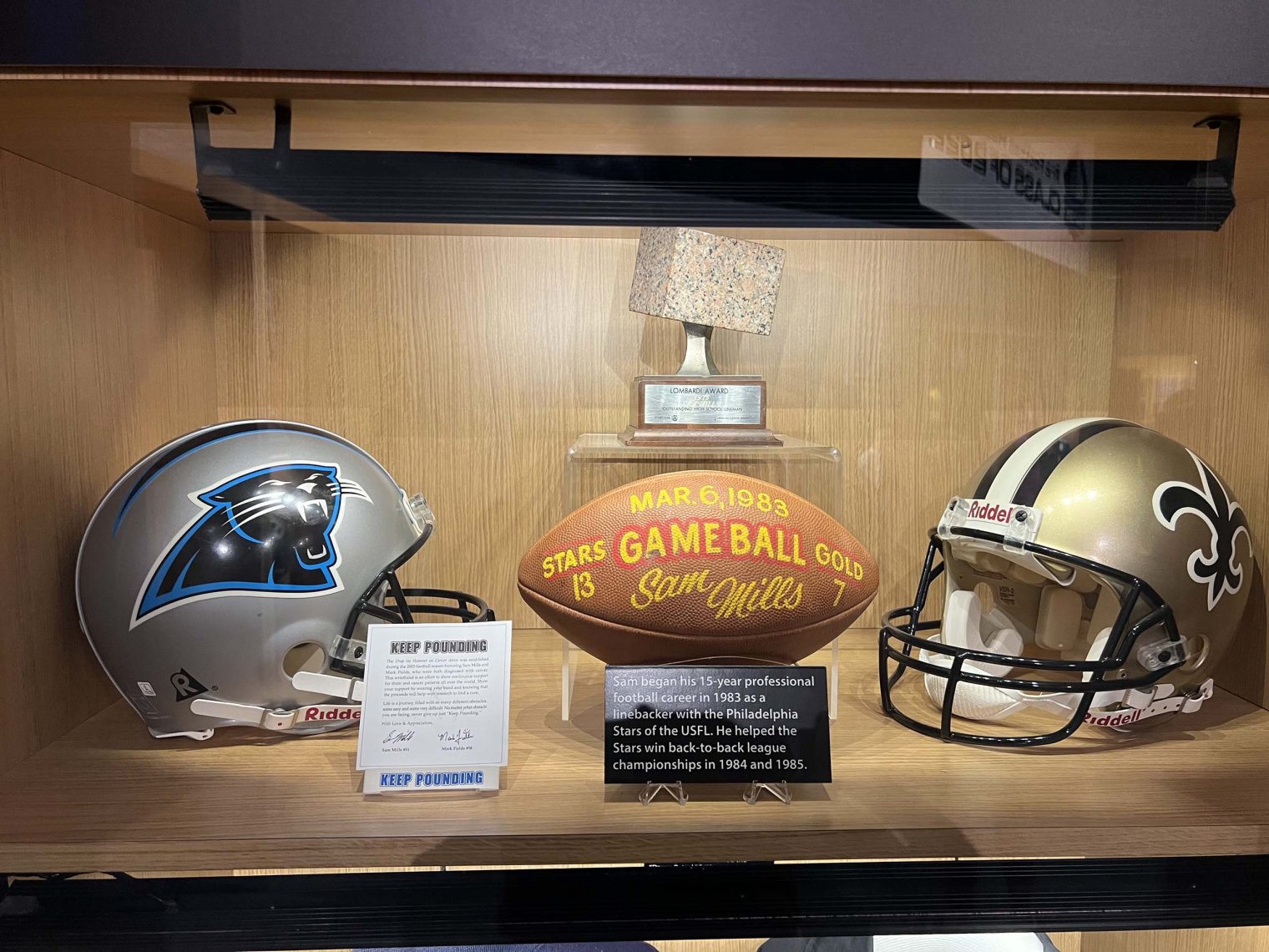 two helmets, a trophy, and a football in a glass case