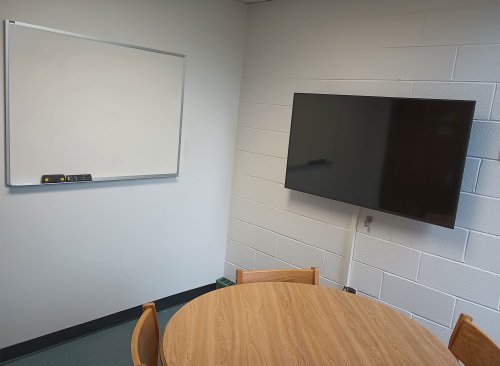 a desk with 4 chairs, a whiteboard and monitor
