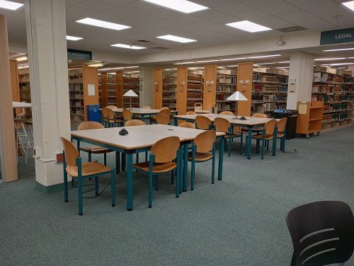 a study space with multiple desks and chair with book stacks in the background 