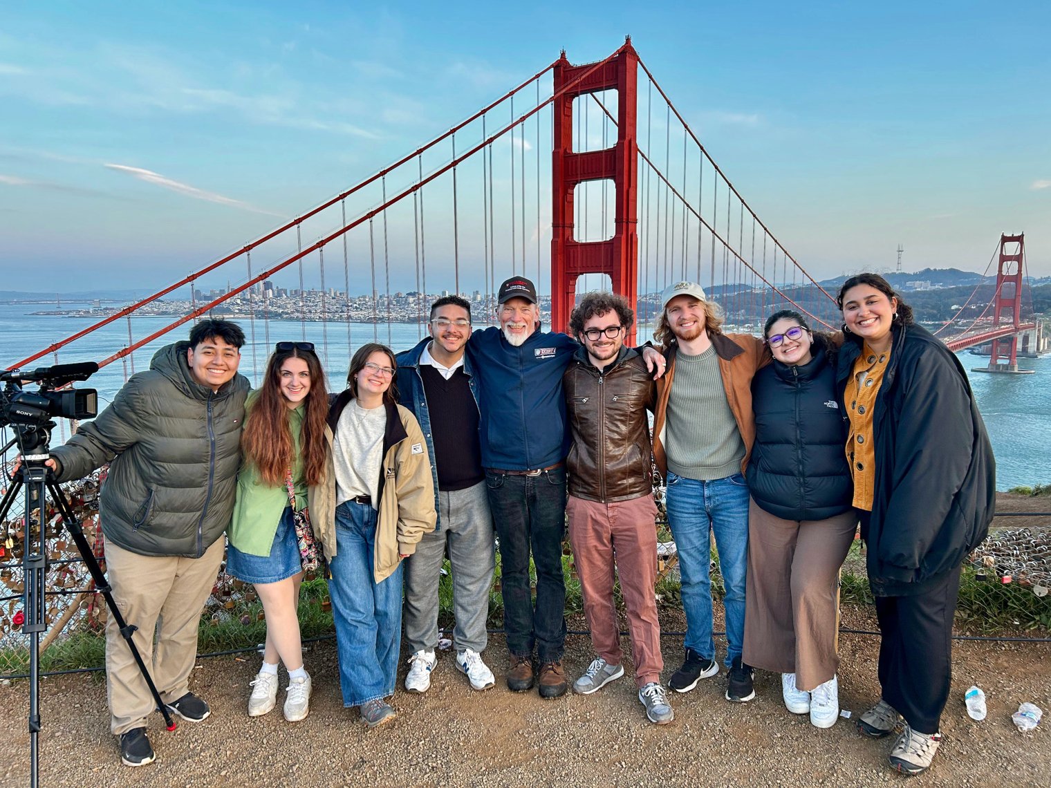 A group of Montclair student journalists stands with News Producer Steve McCarthy in San Francisco, with the iconic Golden Gate Bridge visible in the background.
