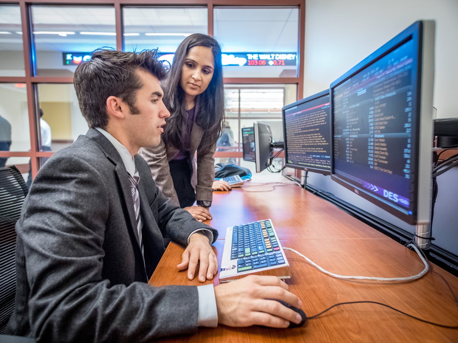 A student using a computer and a faculty member looking on.