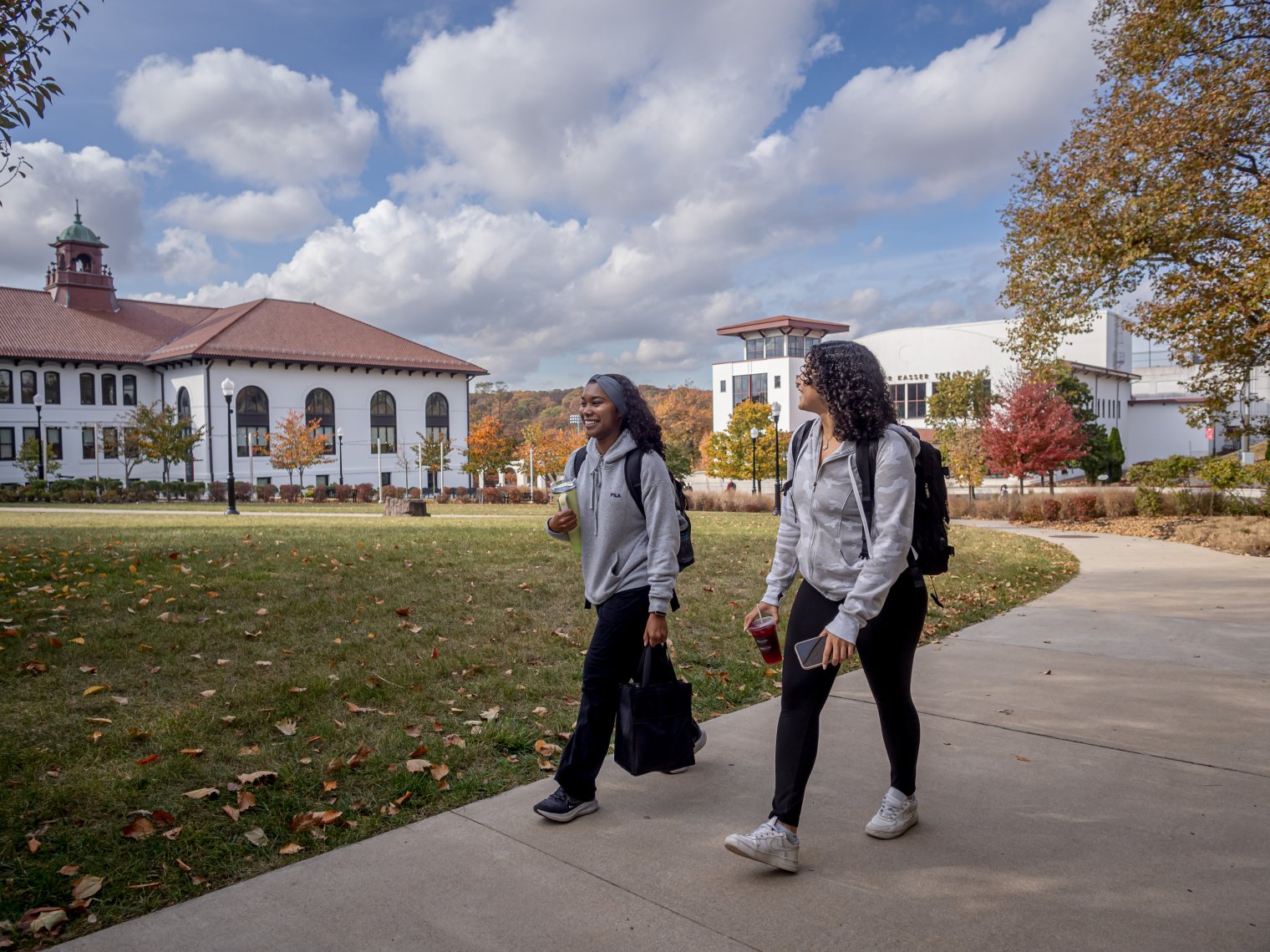Two students walking on campus, campus building in background.
