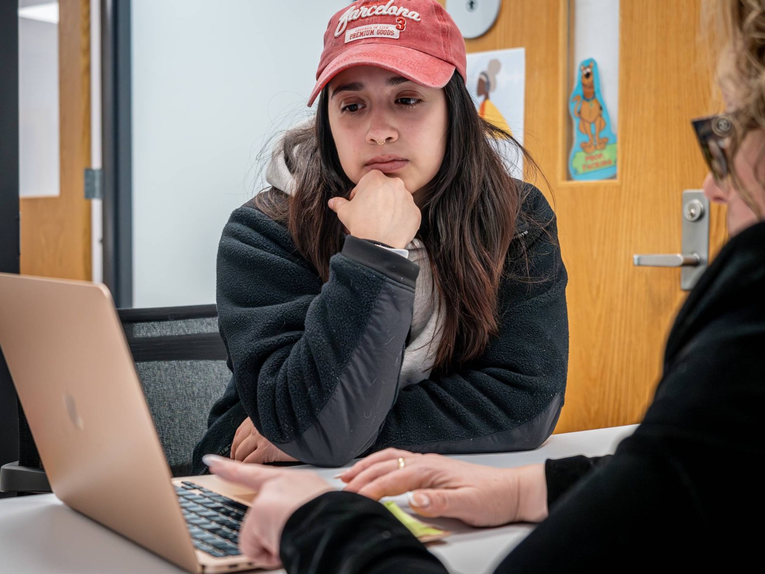 A college student sits in an office and studies a laptop screen