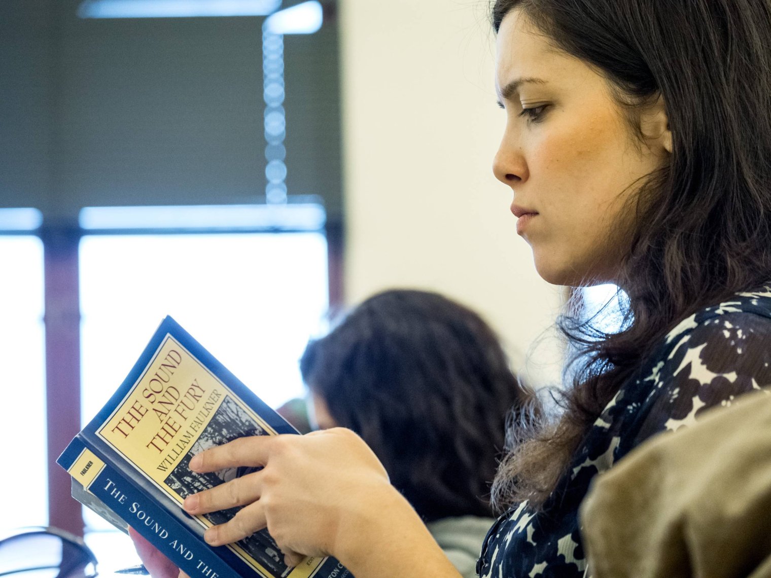 Student reading a copy of the Sound and the Fury in a classroom