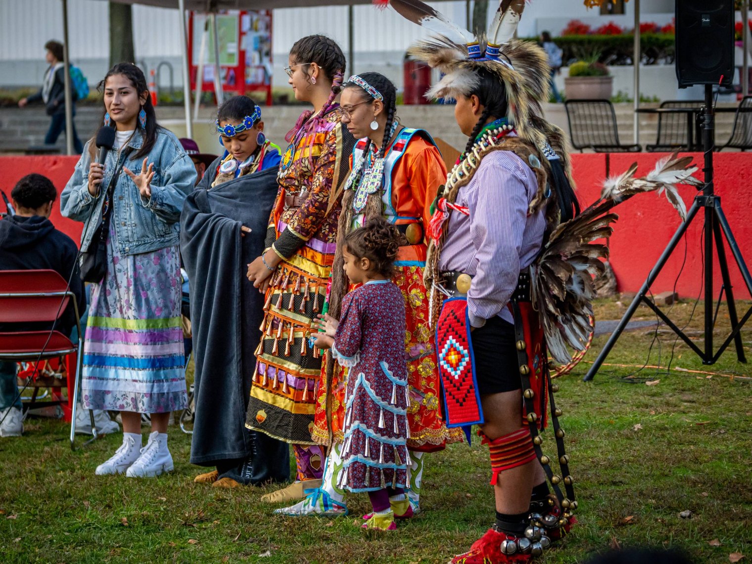 A small group of indigenous people in traditional regalia standing together while one person speaks